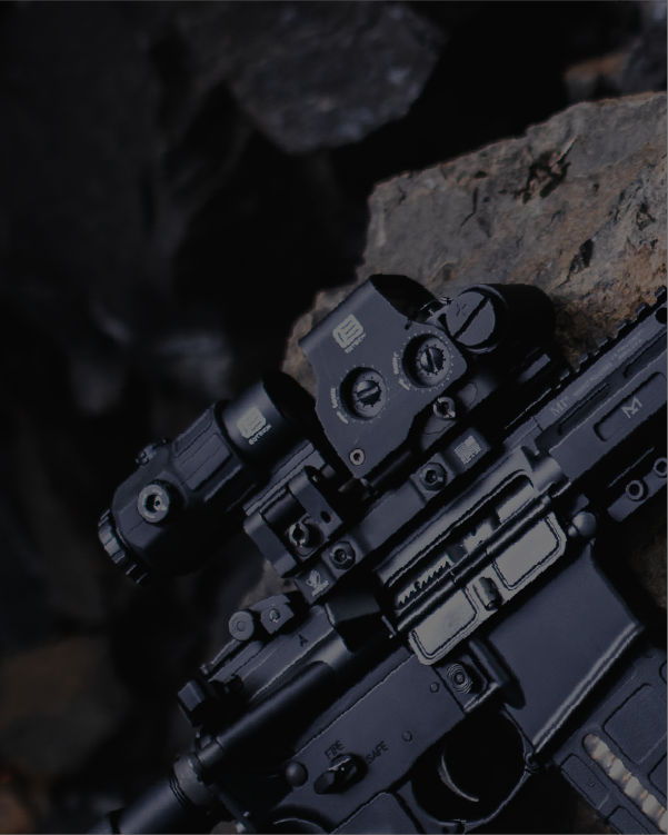 Close-up of a rifle with black EOTECH HWS and maginifier on a rocky background