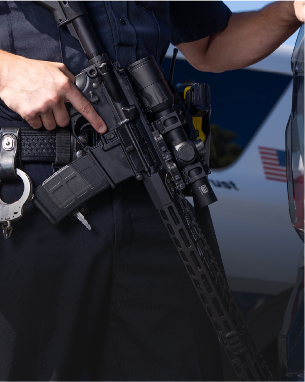 Person holding a rifle with a EOTECH Vudu black scope and  police vehicle in the background