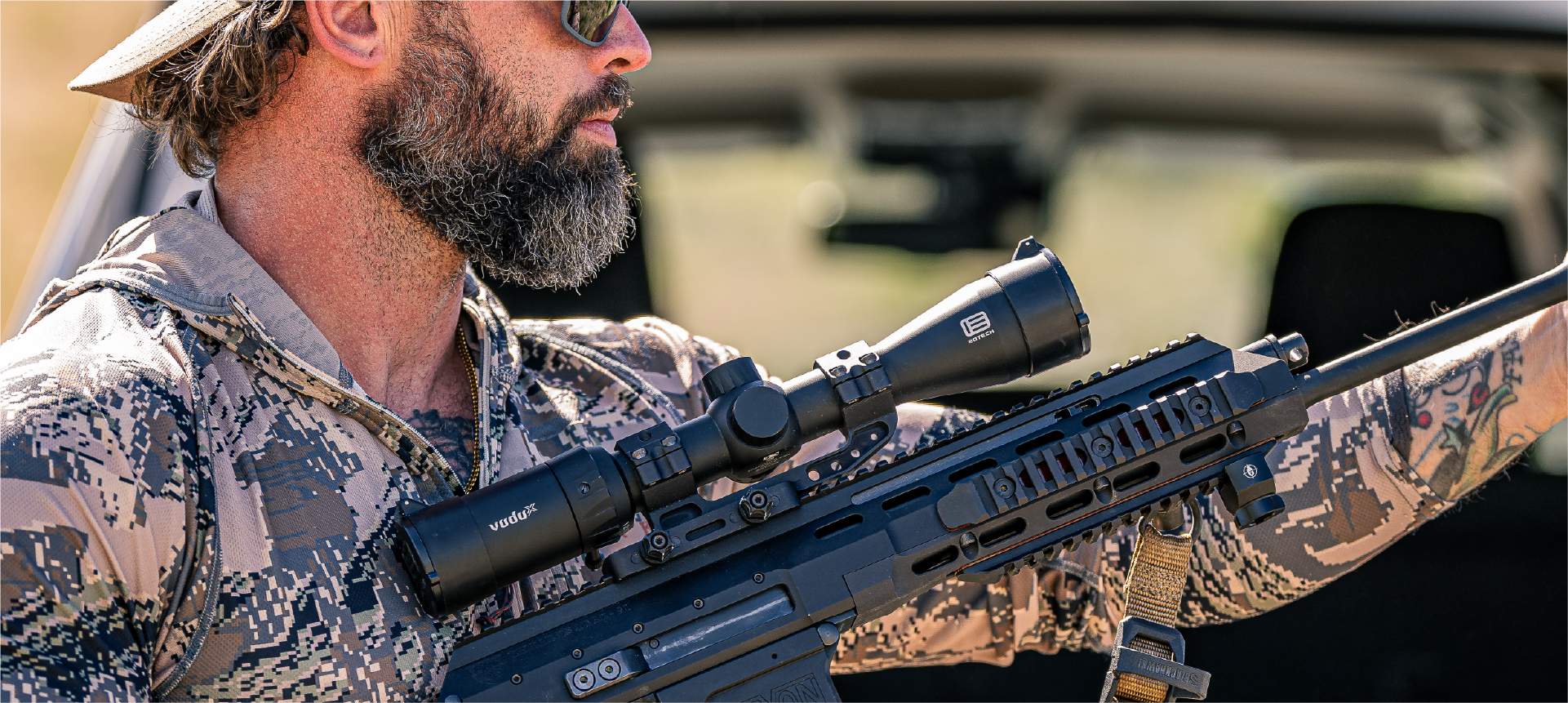 Man in camouflage holding a rifle with a EOTECH Vudu scope, outdoors.