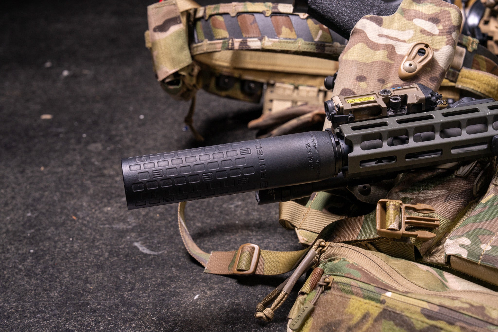 Close-up of a tactical rifle with a EOTECH DCBL black suppressor on camouflage gear.