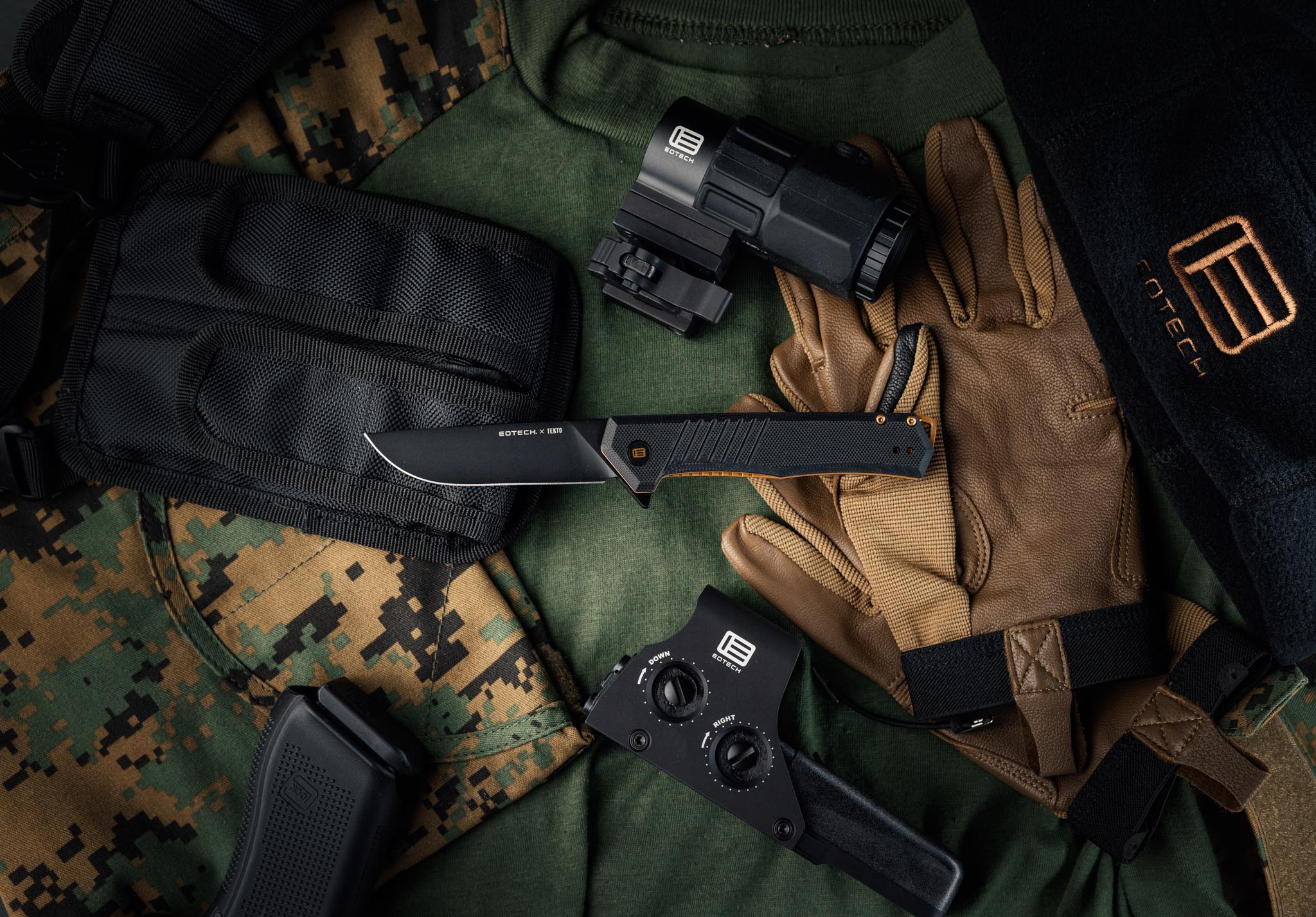Assorted tactical gear including a EOTECH  knife, G45 magnifier, HWS and gloves on a camouflage surface.