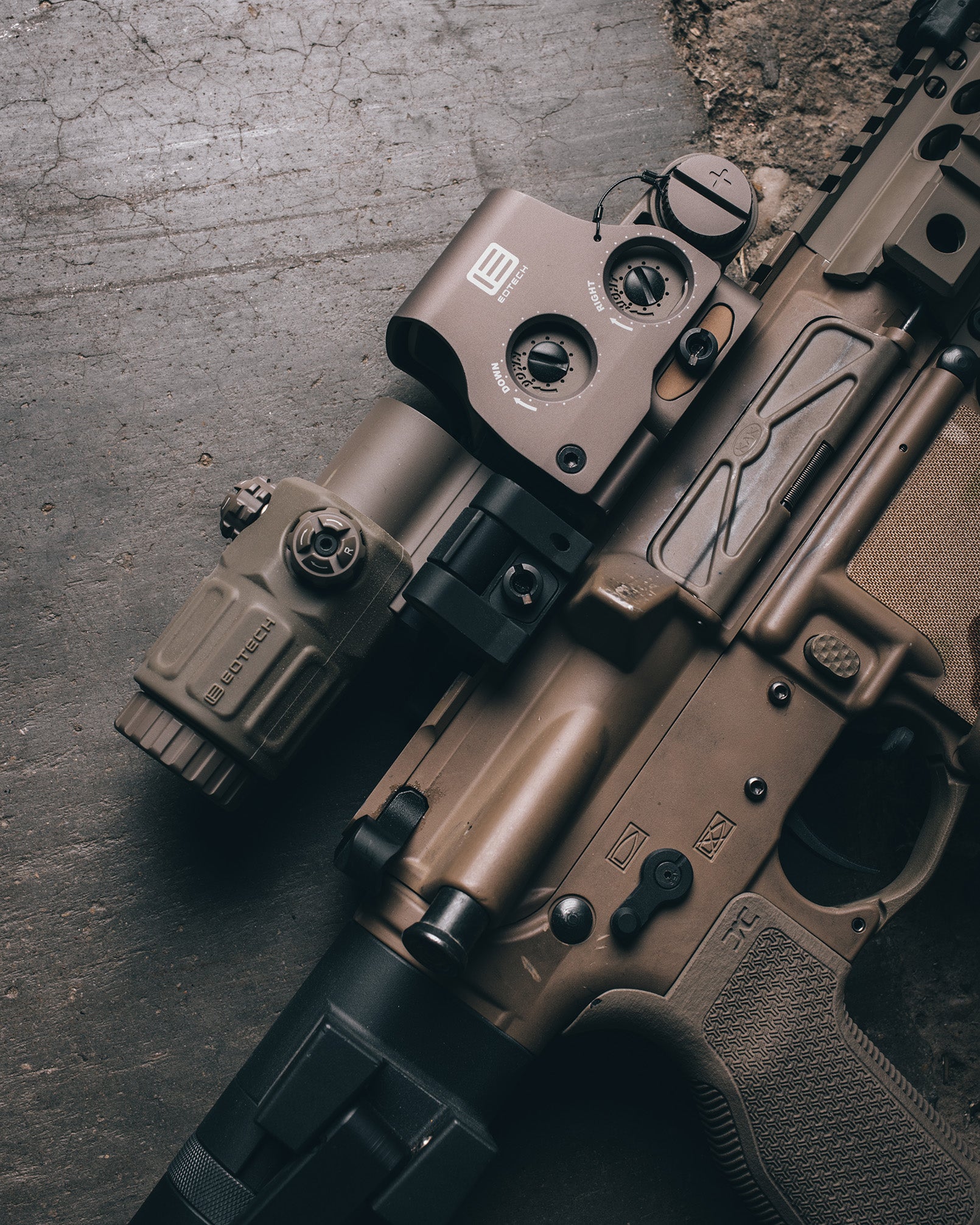 Close-up of a rifle with tan EOTECH HWS and magnifier on a textured surface
