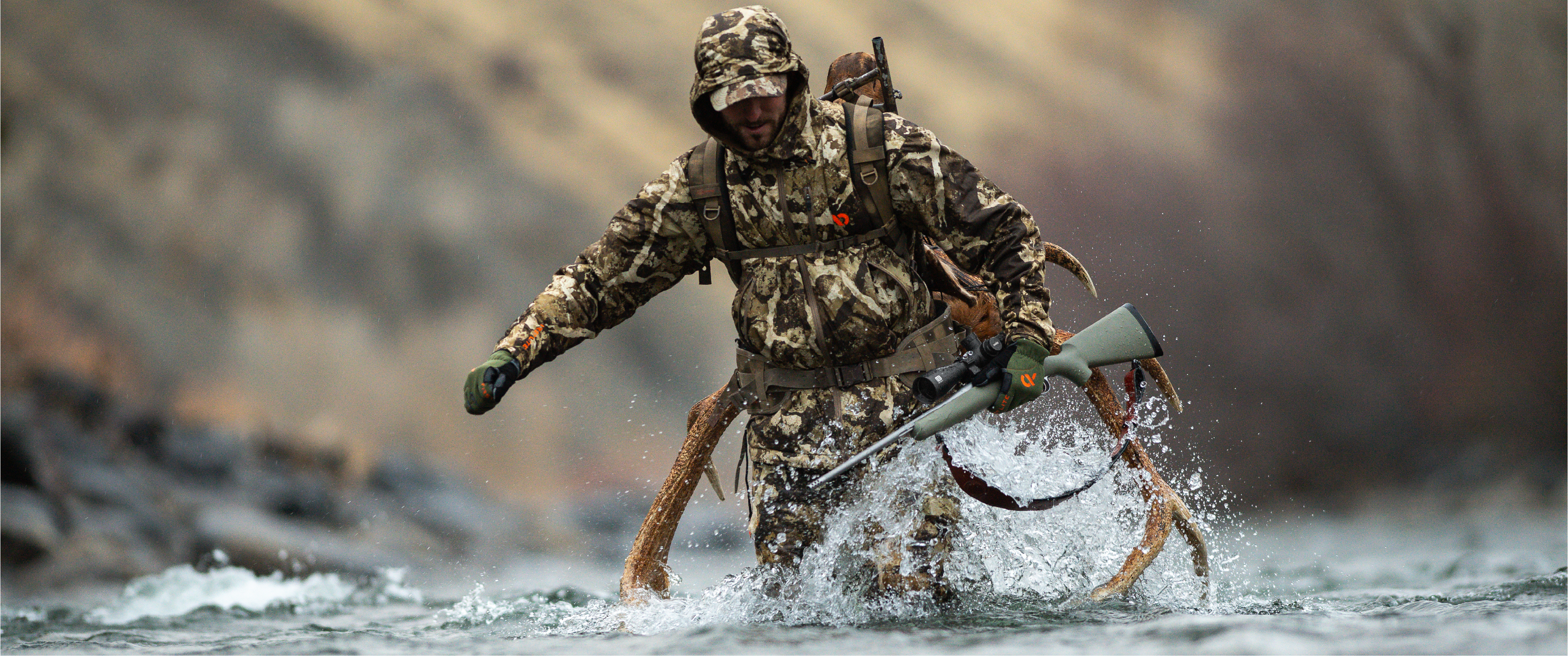 Hunter in camouflage gear walking through water with a rifle and EOTECH Vudu scope